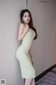 A woman in a green dress leaning against a wall.