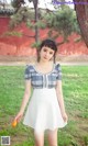 A woman in a white dress standing next to a tree.