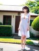 A woman in a white dress standing in front of a house.