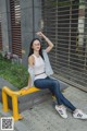 A woman sitting on a yellow bench in front of a building.