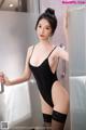 A woman in a black bodysuit and stockings leaning against a wall.