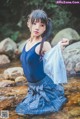 A woman in a blue top and plaid skirt standing in a stream.