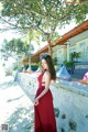 A woman in a red dress leaning against a wall.