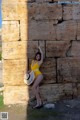 A woman in a yellow bathing suit leaning against a stone wall.