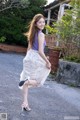 A woman in a purple top and a white skirt is walking down the street.